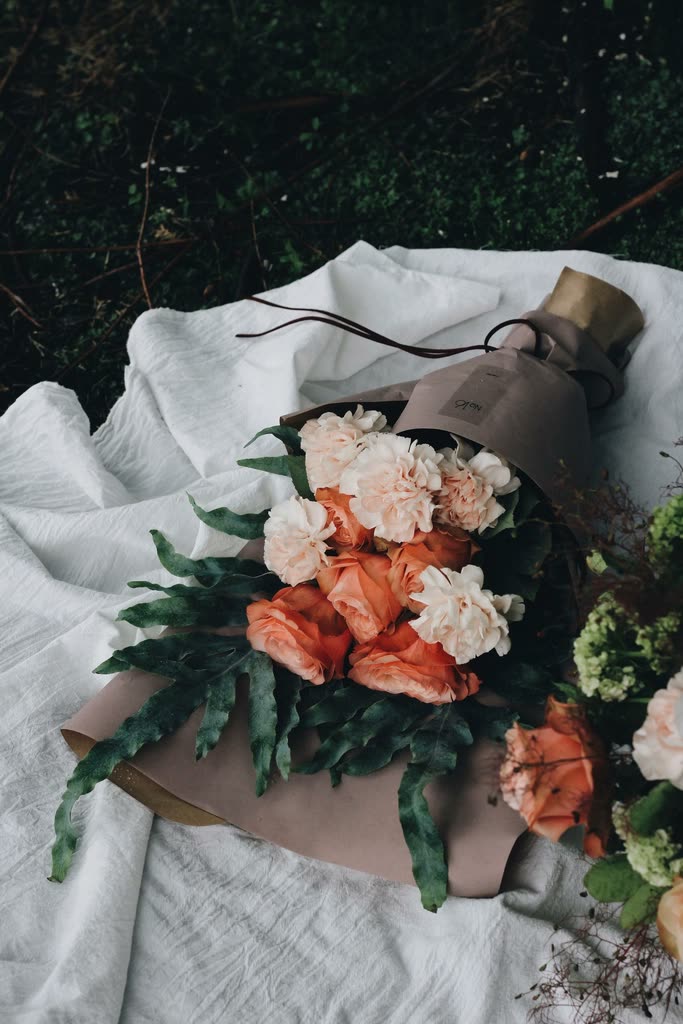 Pale carnations, peach roses and greenery in a brown paper wrap