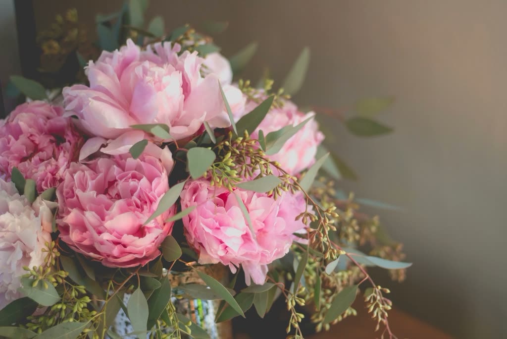 A glass vase filled with pink peonies and green foliage