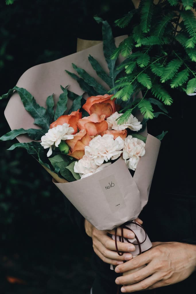 A person holding white carnations with peach roses and greenery